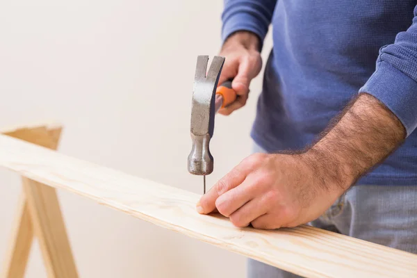 Casual man hammering nail in plank — Stock Photo, Image