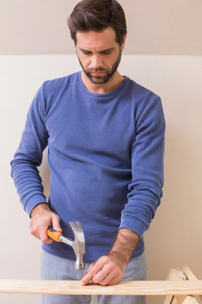 Casual man hammering nail in plank — Stock Photo, Image