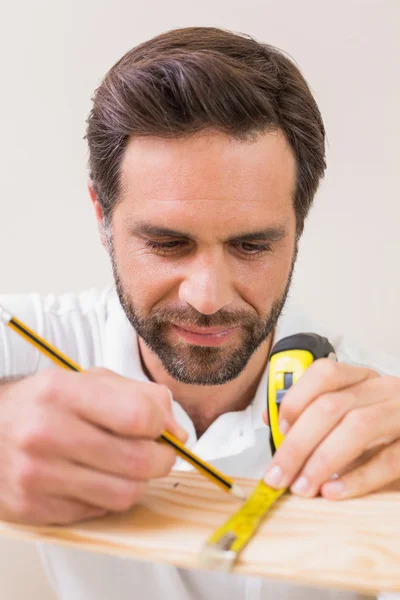 Casual man measuring plank of wood — Stock Photo, Image