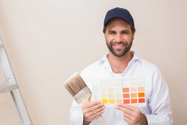 Pintor sosteniendo una carta de colores sonriendo a la cámara — Foto de Stock