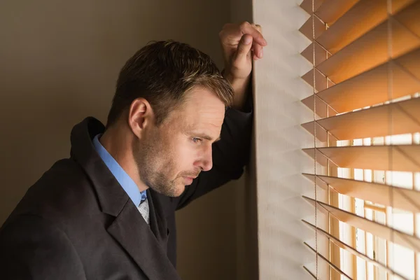 Serious businessman peeking through blinds — Stock Photo, Image