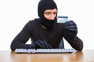 Burglar typing on keyboard and holding credit card clipart