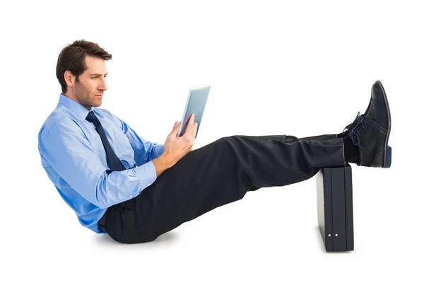 Businessman sitting using tablet with feet on his briefcase — Stock Photo, Image