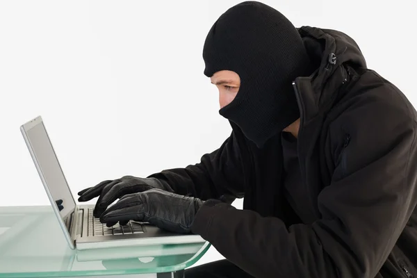 Грабитель, сидящий за столом и взламывающий ноутбук — стоковое фото