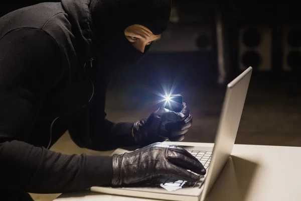 Räuber hackt Laptop, während er mit Handy Licht macht — Stockfoto