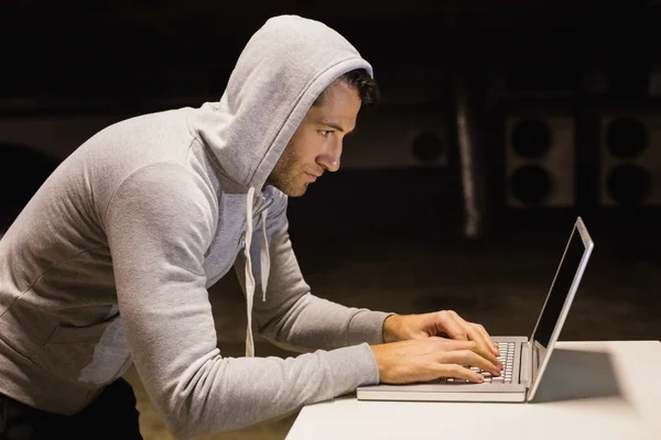 Man in hood jacket hacking a laptop — Stock Photo, Image