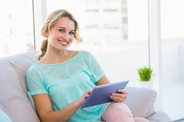 Sorrindo casual loira sentada no sofá usando tablet — Fotografia de Stock