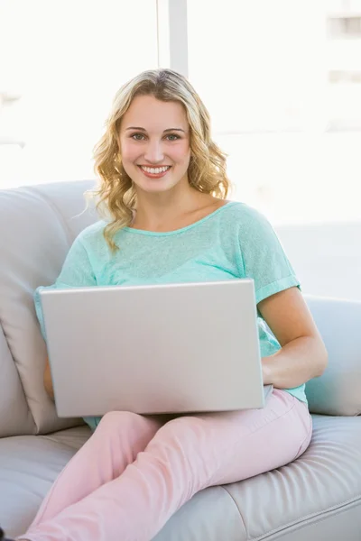 Smiling casual blonde sitting on couch using laptop — Stock Photo, Image