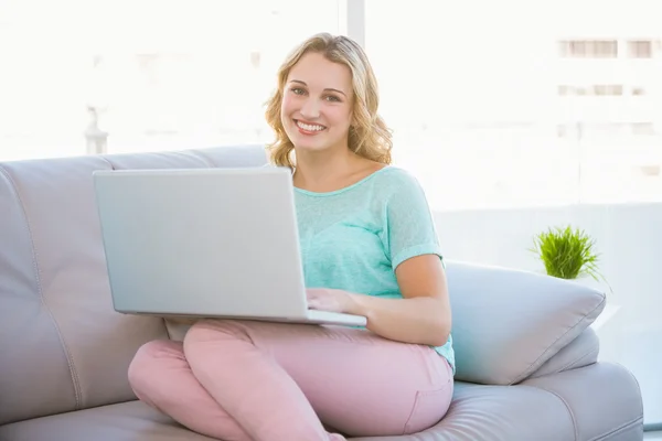 Happy casual blonde relaxing on couch using laptop — Stock Photo, Image