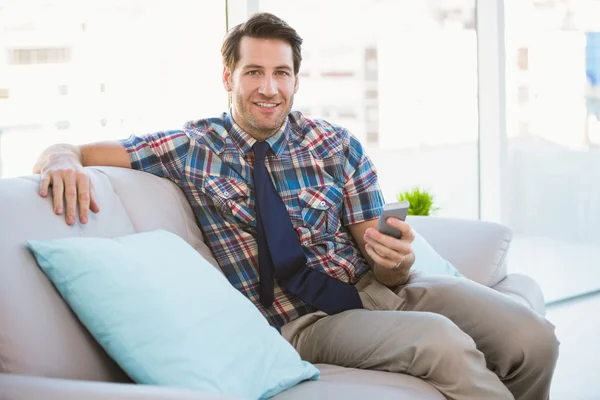 Hombre feliz sentado en el sofá enviando un mensaje de texto —  Fotos de Stock