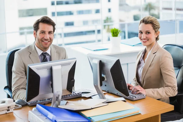 Geschäftsleute benutzen Computer, während sie in die Kamera schauen — Stockfoto