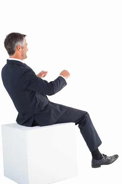 Улыбающийся бизнесмен сидит на кубе — стоковое фото