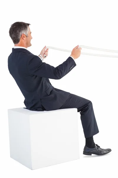 Businessman sitting on a cube and holding rope — Stock Photo, Image