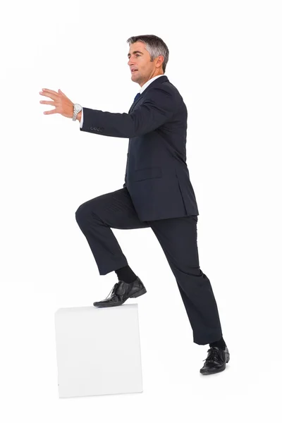 Businessman climbing on a cube with arms out — Stock Photo, Image