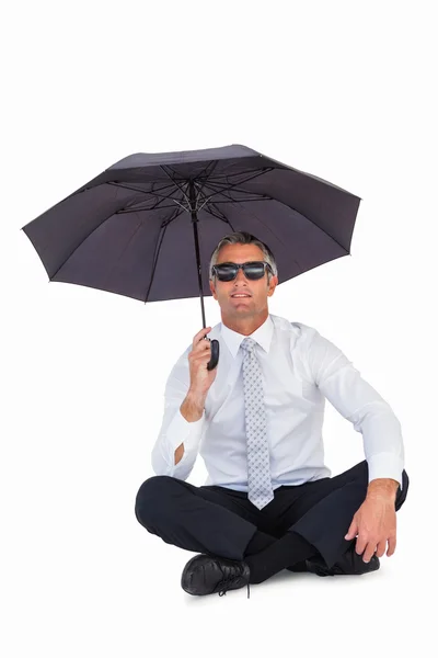 Businessman wearing sunglasses and sheltering with umbrella — Stock Photo, Image