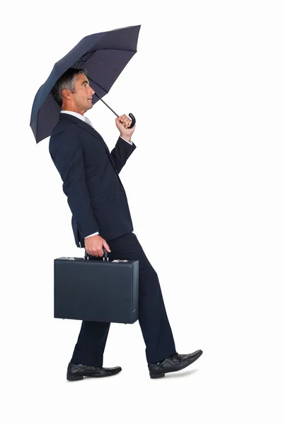 Businessman walking and holding briefcase under umbrella — Stock Photo, Image