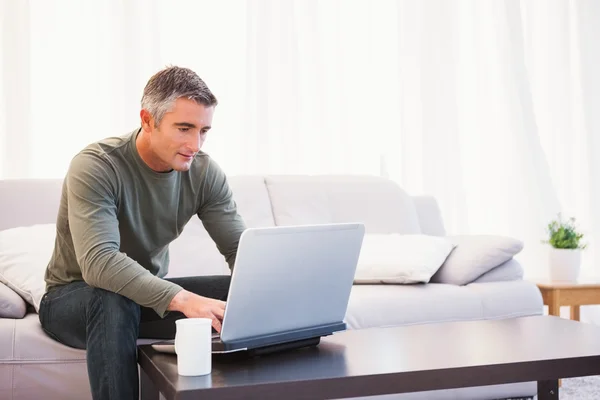 Homem alegre sentado no sofá usando laptop — Fotografia de Stock