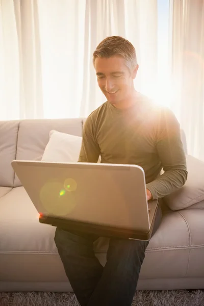 Glimlachende man zit op de Bank met behulp van laptop — Stockfoto