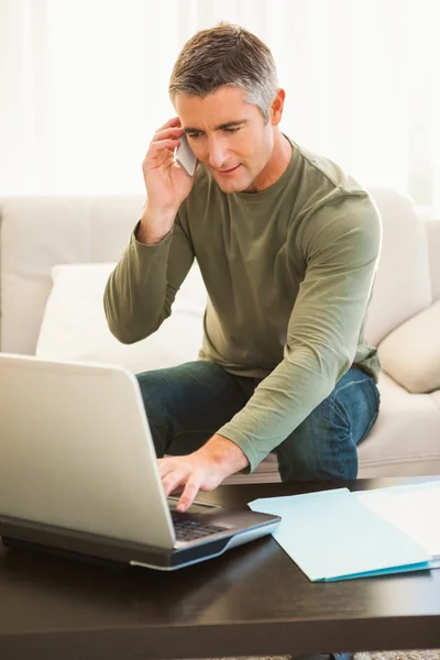 Adam kanepede oturan ve dizüstü bilgisayar kullanarak telefon — Stok fotoğraf