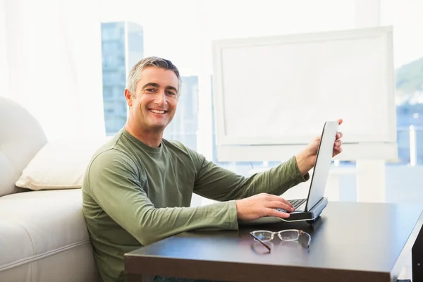 Homme souriant utilisant un ordinateur portable avec des lunettes sur la table — Photo