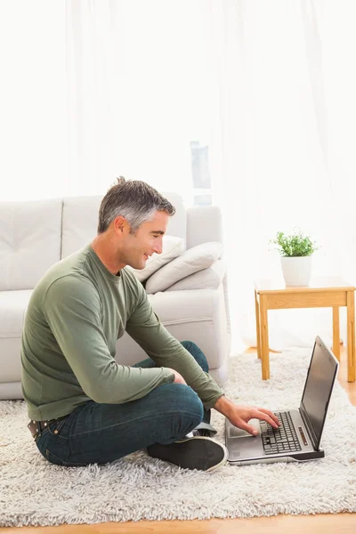 Smiling man sitting on carpet using laptop — Stock Photo, Image