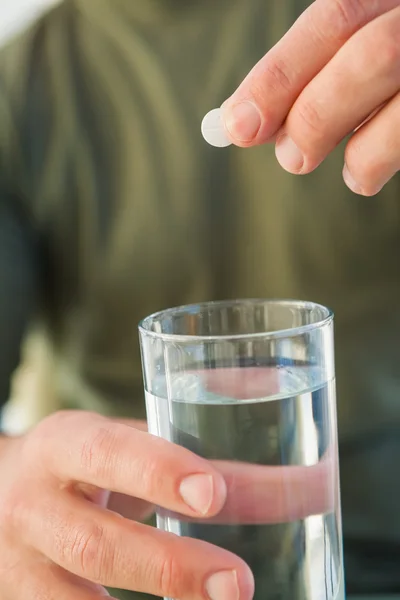 Primo piano di un uomo che tiene un bicchiere d'acqua e una pillola — Foto Stock