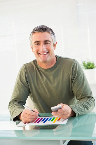Smiling man analyzing chart and holding mobile phone — Stock Photo, Image