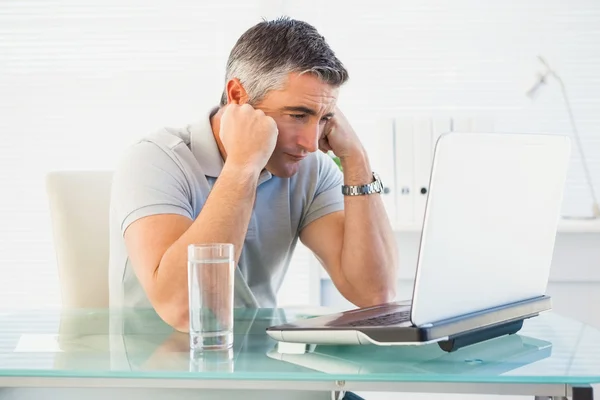 Hombre cansado sentado y mirando su portátil — Foto de Stock