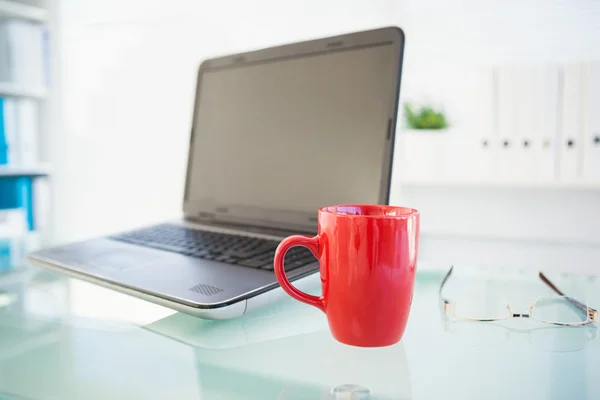 Laptop på bord med röd mugg och glasögon — Stockfoto