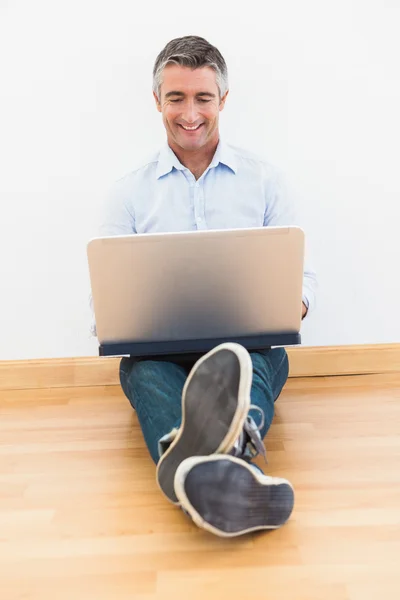 Homem feliz sentado em parquet usando laptop — Fotografia de Stock