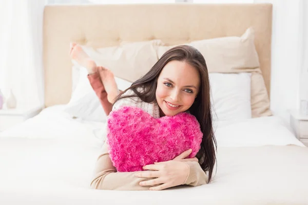 Mooie brunette houden hart kussen op bed — Stockfoto