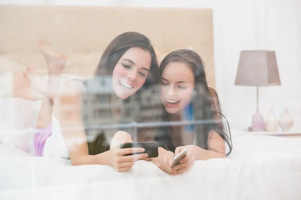 Bonitos amigos mirando el teléfono inteligente en la cama —  Fotos de Stock