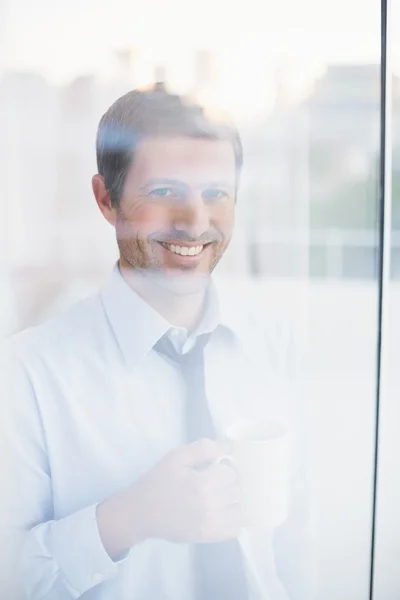 Usměvavý obchodník drží hrnek při pohledu z okna — Stock fotografie