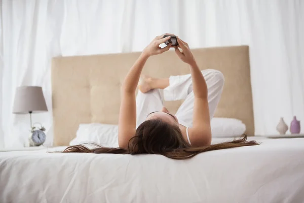 Půvabná brunetka odesílání textu na posteli — Stock fotografie