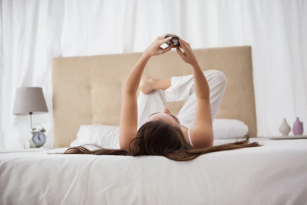 Mooie brunette verzenden van een tekst op bed — Stockfoto