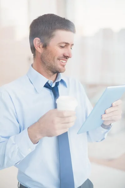 Sonriente hombre de negocios usando la tableta que sostiene la taza desechable visto thr — Foto de Stock