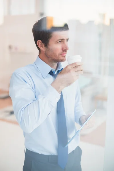 Empresario sosteniendo taza y tableta desechables mirando hacia fuera el wi —  Fotos de Stock