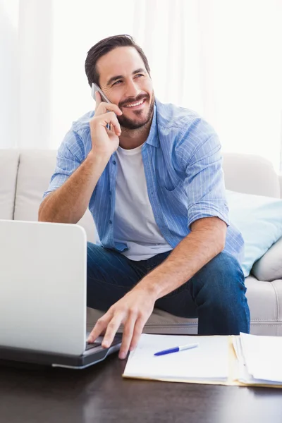 Man paying his bills with laptop while talking on phone — Stock Photo, Image