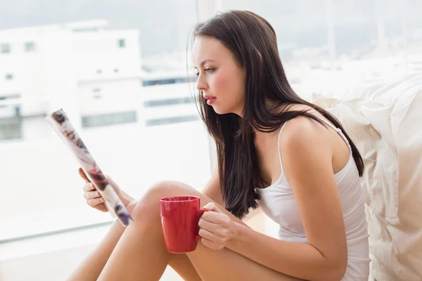 Ładna brunetka siedzi na podłodze czytania magazynu — Zdjęcie stockowe