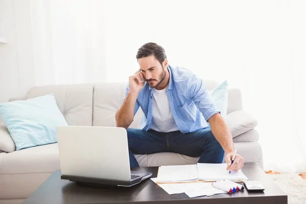 Homem pagando suas contas com laptop enquanto fala no telefone — Fotografia de Stock