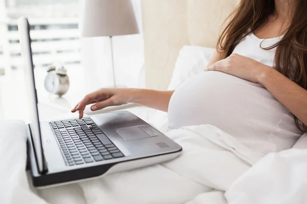 Έγκυος μελαχρινή χρησιμοποιώντας φορητό υπολογιστή στο κρεβάτι — Φωτογραφία Αρχείου