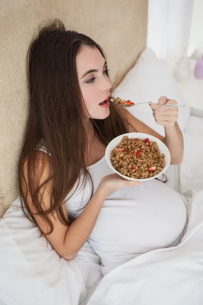 Bruna incinta che mangia cereali a letto — Foto Stock