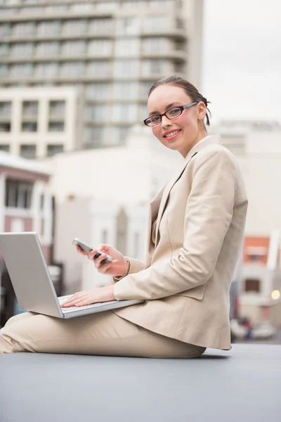 Jonge zakenvrouw met behulp van laptop houden haar telefoon — Stockfoto