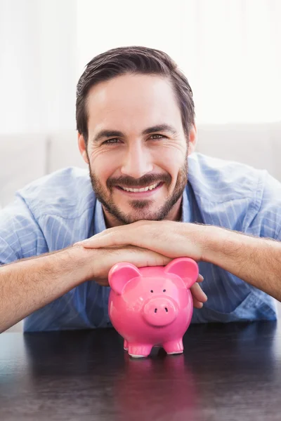 Lächelnder Mann legt sich aufs Sparschwein — Stockfoto