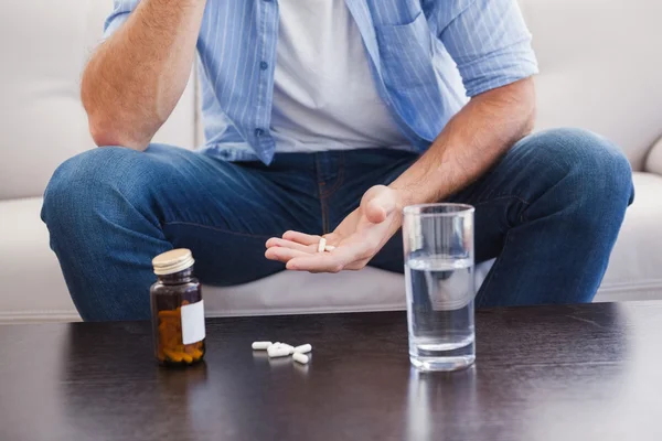 El hombre tomando sus pastillas en el sofá — Foto de Stock