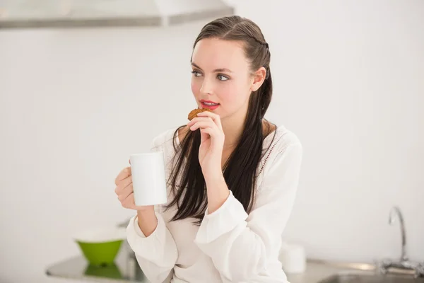 Pretty brunette holding a mug and cookie — Stock Photo, Image