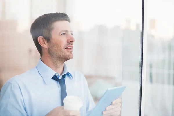 Empresario sosteniendo taza y tableta desechables mirando hacia fuera el wi — Foto de Stock