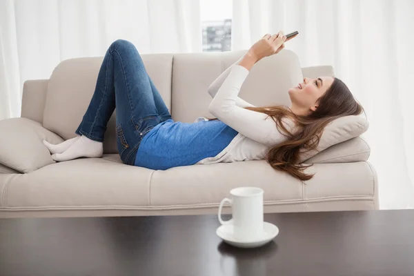 Hübsche Brünette schickt einen Text auf die Couch — Stockfoto