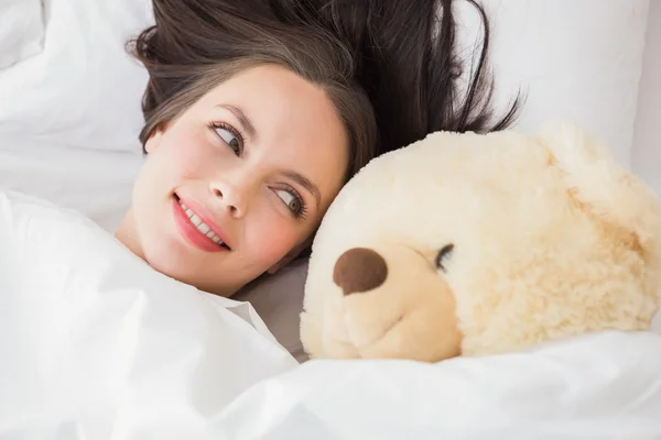 Mooie brunette onder het dekbed met teddy bear — Stockfoto