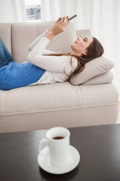 Pretty brunette sending a text on the couch — Stock Photo, Image